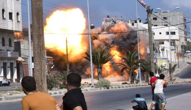 Palestinian men look on as a bomb from an Israeli air strike hits a house in Gaza City on August 23,